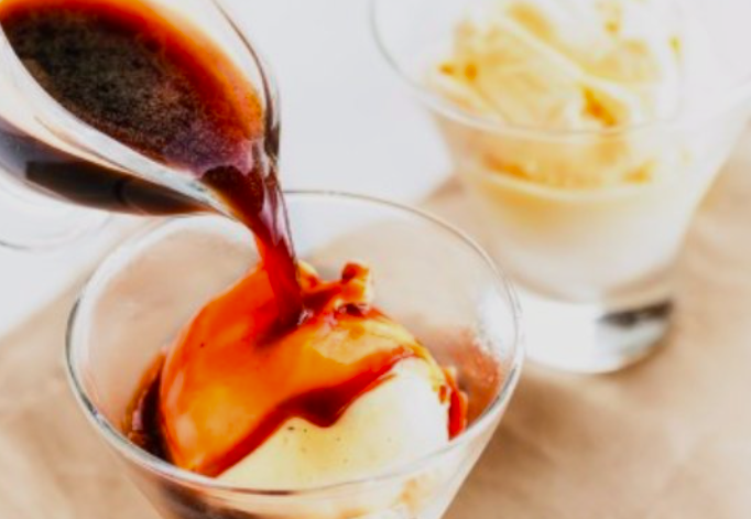 Espresso quente sendo despejado sobre uma bola de sorvete de baunilha em uma taça de vidro, com a calda escura escorrendo pelo sorvete, e uma segunda taça com sorvete ao fundo levemente desfocada.